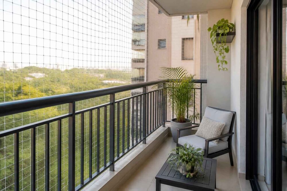 Balkon z czarną balustradą, roślinami, fotelem i stolikiem z widokiem na zieloną okolicę