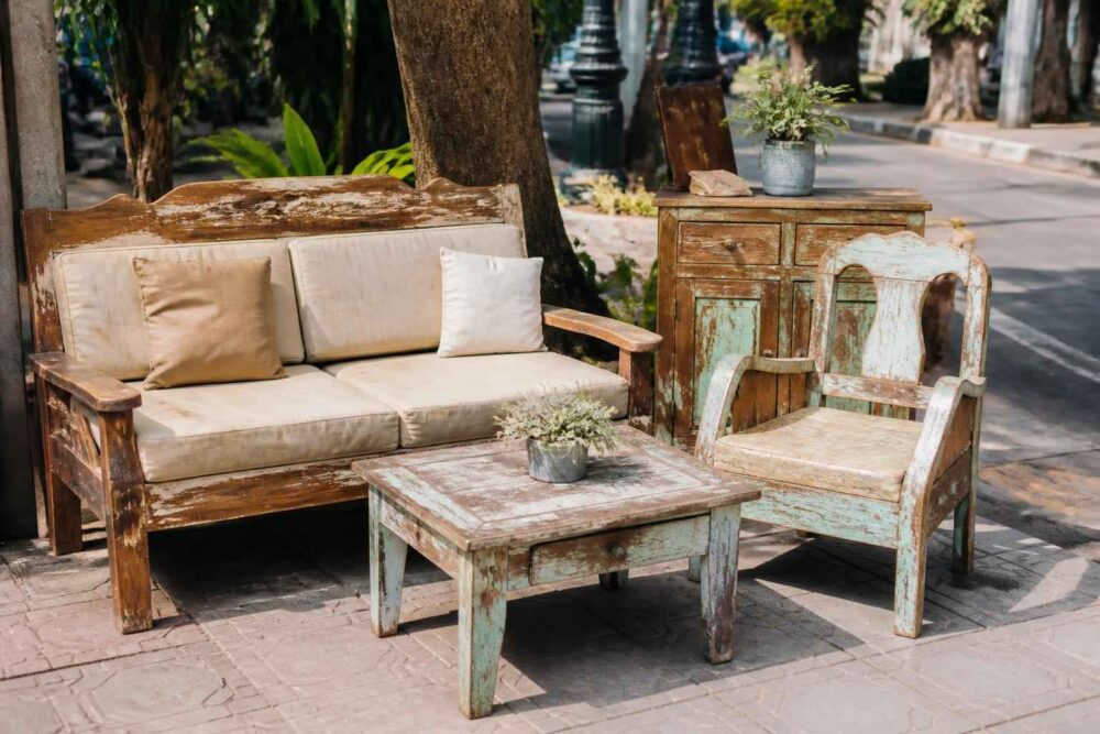 Drewniana sofa, fotel i stolik z doniczką ustawione na miejskim chodniku wśród drzew